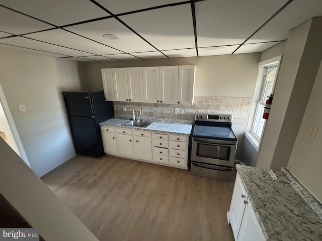 kitchen with electric range, white cabinets, freestanding refrigerator, and a sink