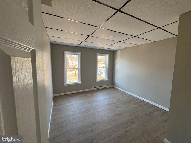 empty room with baseboards, a paneled ceiling, wood finished floors, and a baseboard radiator