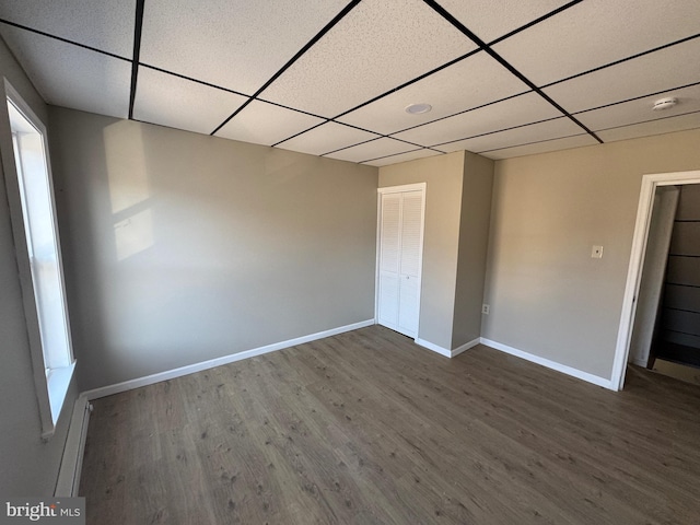 unfurnished bedroom with wood finished floors, baseboards, a closet, and a paneled ceiling