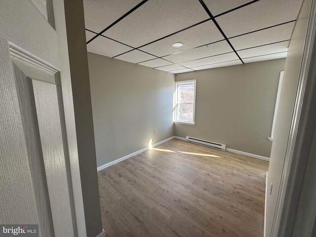 empty room featuring a drop ceiling, baseboards, baseboard heating, and wood finished floors