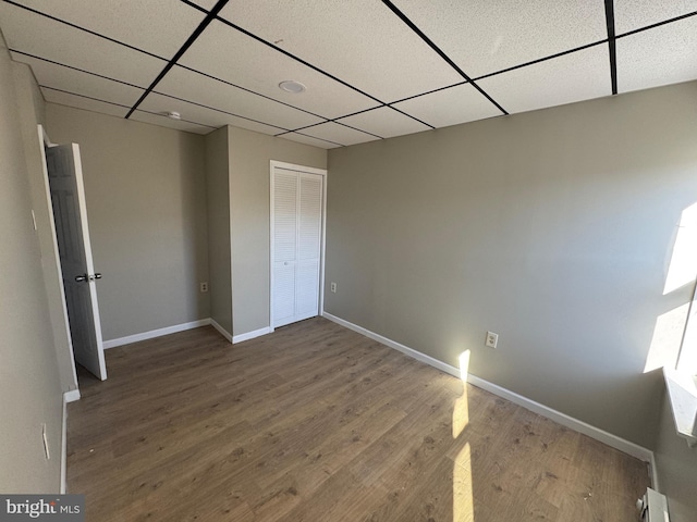 unfurnished bedroom featuring baseboards, wood finished floors, a closet, and a paneled ceiling