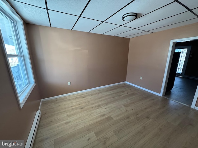 spare room with a drop ceiling, baseboards, baseboard heating, and wood finished floors