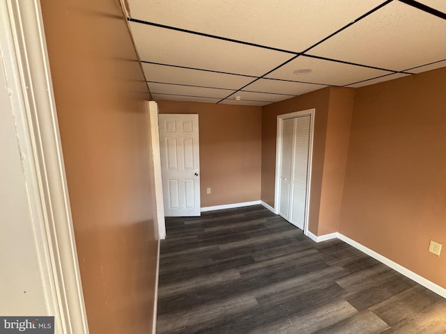 empty room with a drop ceiling, baseboards, and dark wood-style floors