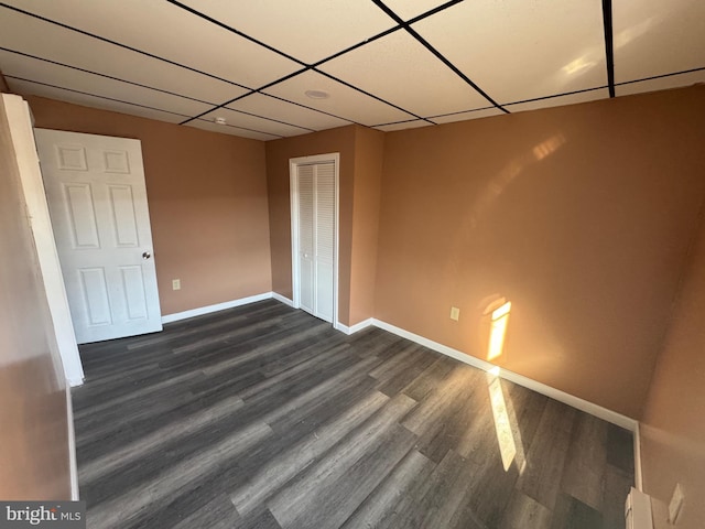 unfurnished bedroom with a drop ceiling, a closet, baseboards, and dark wood finished floors