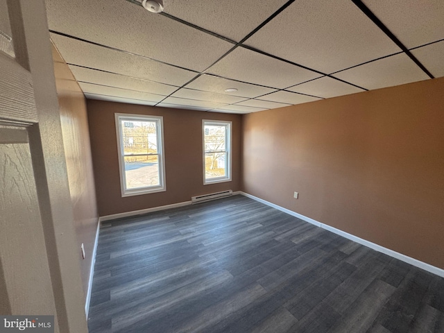 unfurnished room featuring a baseboard heating unit, a paneled ceiling, dark wood-type flooring, and baseboards