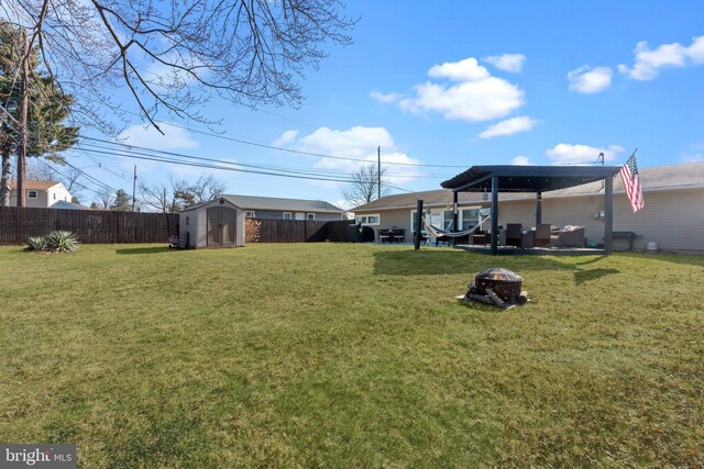 view of yard with a storage unit, an outdoor structure, a fenced backyard, and an outdoor fire pit