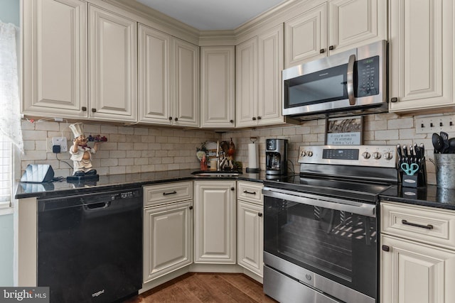 kitchen featuring dark wood-style floors, dark stone counters, appliances with stainless steel finishes, cream cabinets, and backsplash