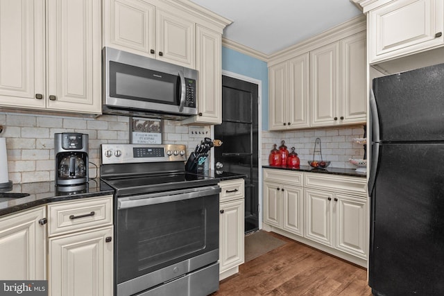 kitchen featuring backsplash, dark stone countertops, cream cabinets, wood finished floors, and stainless steel appliances