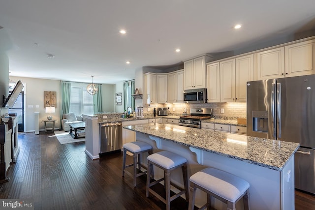 kitchen featuring light stone countertops, a peninsula, dark wood-style flooring, appliances with stainless steel finishes, and tasteful backsplash