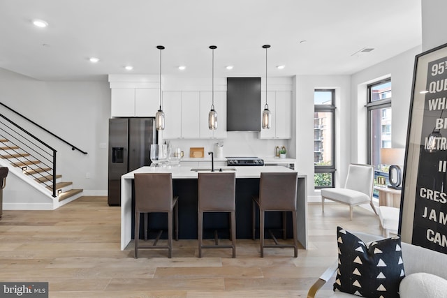 kitchen featuring an island with sink, light countertops, light wood-style flooring, stainless steel refrigerator with ice dispenser, and white cabinets