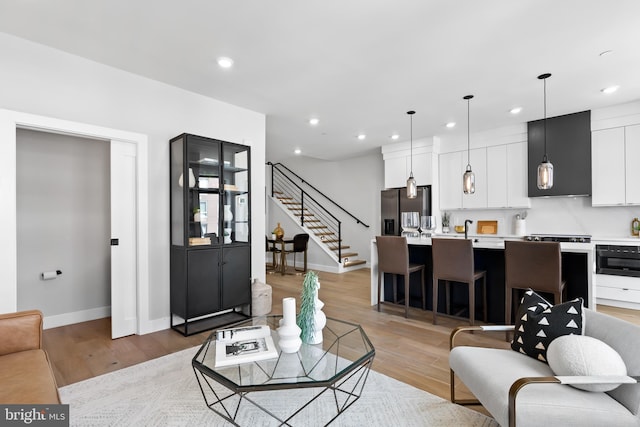 living room featuring recessed lighting, light wood-style flooring, and stairs