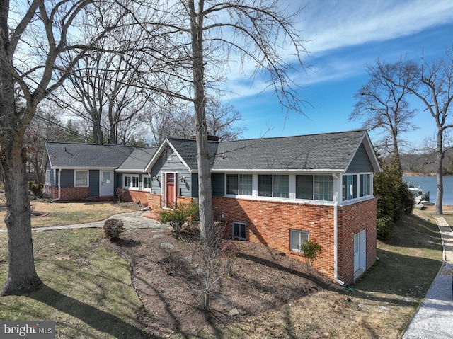 ranch-style home featuring a water view, brick siding, driveway, and a shingled roof