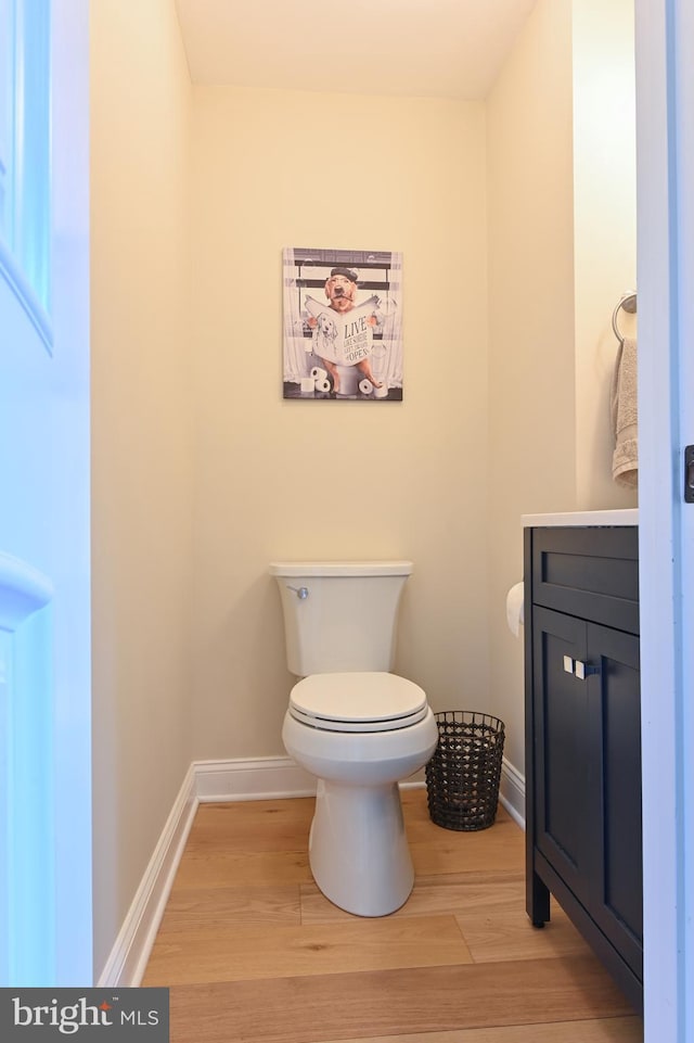 half bath featuring vanity, toilet, wood finished floors, and baseboards