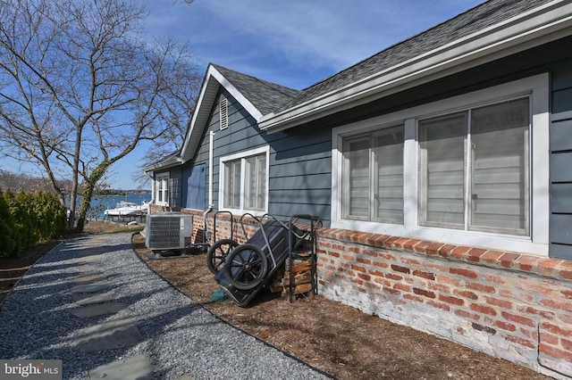 view of side of home with cooling unit and a shingled roof