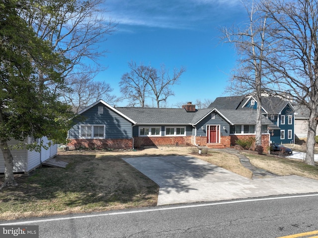 view of front of property featuring roof with shingles, driveway, a chimney, a front lawn, and brick siding