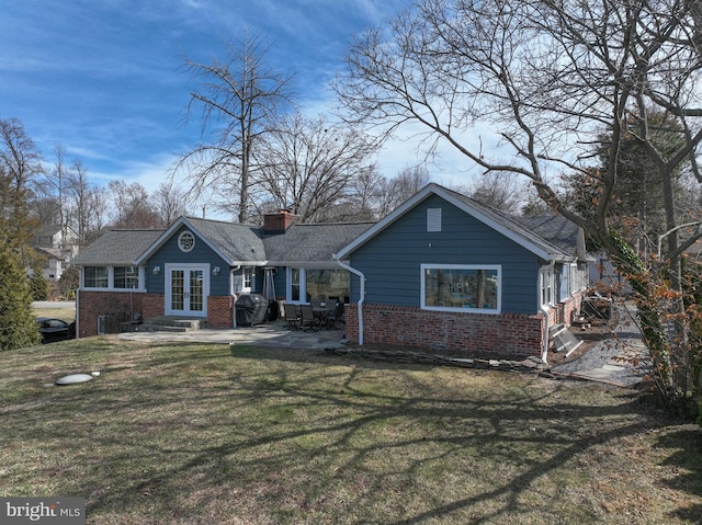 view of front of house featuring french doors, brick siding, a chimney, and a front lawn