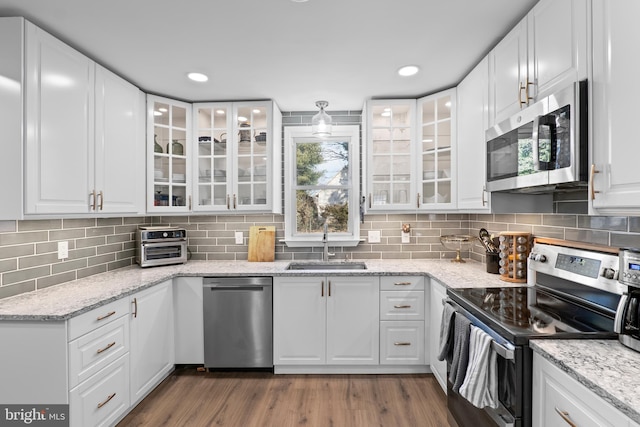 kitchen featuring tasteful backsplash, appliances with stainless steel finishes, wood finished floors, white cabinets, and a sink