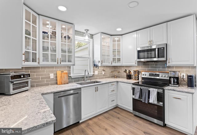 kitchen with a sink, white cabinetry, stainless steel appliances, a toaster, and light wood finished floors