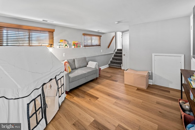 living area with visible vents, baseboards, light wood-style floors, and stairs