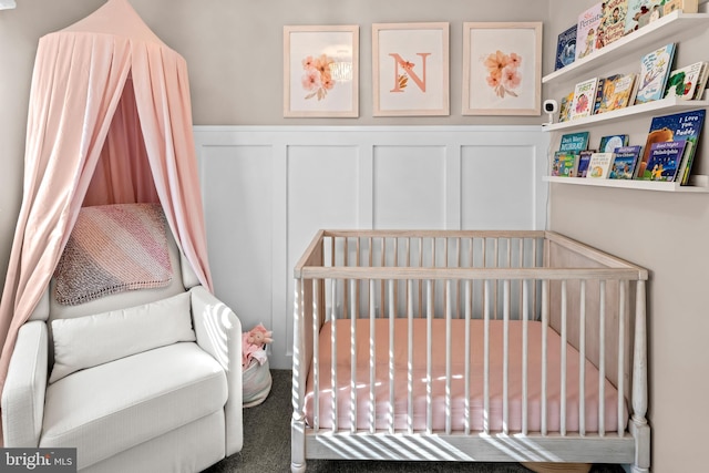 carpeted bedroom with a decorative wall, wainscoting, and a nursery area