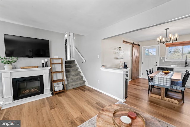 living area with a glass covered fireplace, light wood-style flooring, stairs, and a barn door