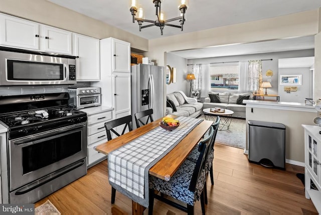 kitchen with open floor plan, light wood-style flooring, stainless steel appliances, a notable chandelier, and white cabinetry