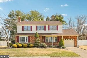 traditional-style home featuring a garage, driveway, a front lawn, and fence