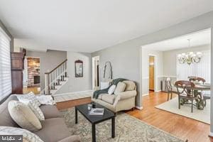 living room with plenty of natural light, an inviting chandelier, wood finished floors, and stairs