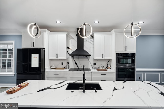 kitchen featuring wall chimney range hood, pendant lighting, an island with sink, white cabinets, and black appliances