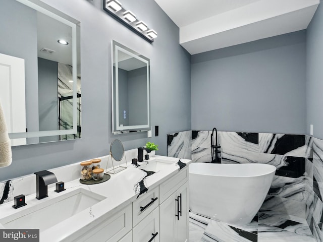 full bathroom featuring double vanity, marble finish floor, a freestanding tub, and a sink