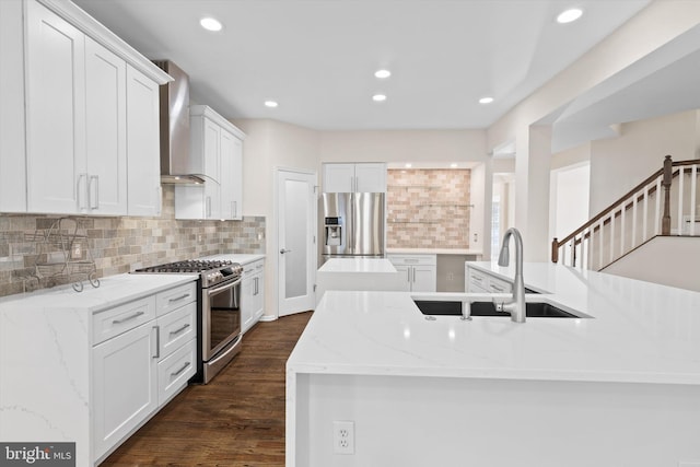 kitchen featuring dark wood finished floors, appliances with stainless steel finishes, white cabinets, wall chimney exhaust hood, and a sink