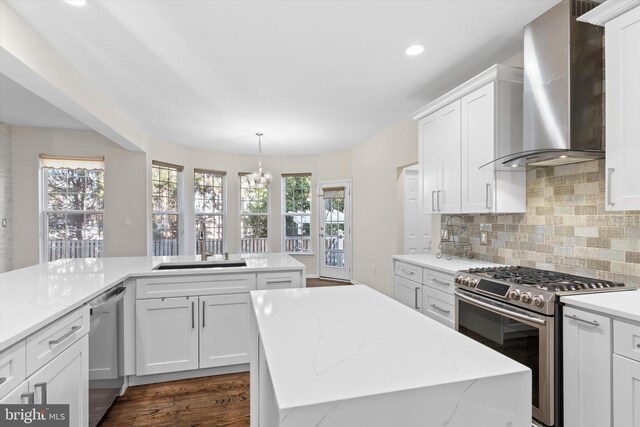 kitchen with a sink, a kitchen island, appliances with stainless steel finishes, wall chimney range hood, and decorative backsplash