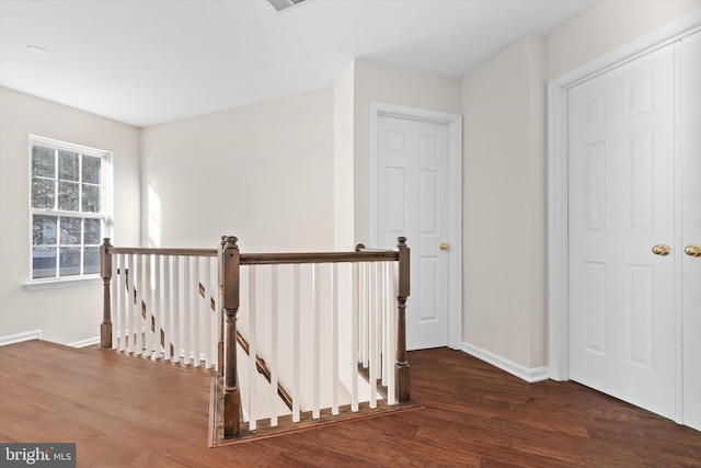 corridor featuring baseboards, an upstairs landing, and wood finished floors