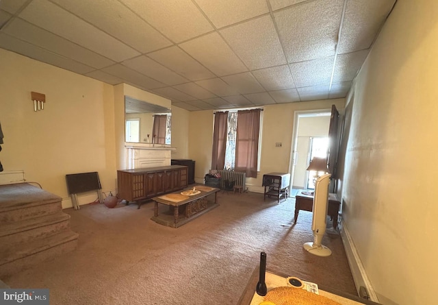 carpeted living area featuring a drop ceiling and baseboards