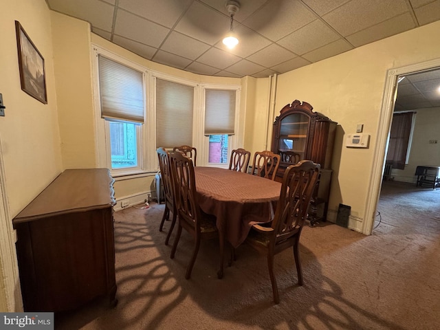 carpeted dining space featuring a drop ceiling and baseboards