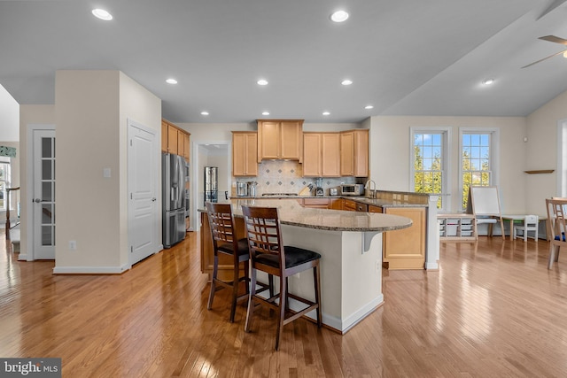 kitchen with tasteful backsplash, a kitchen bar, a peninsula, stone countertops, and stainless steel appliances