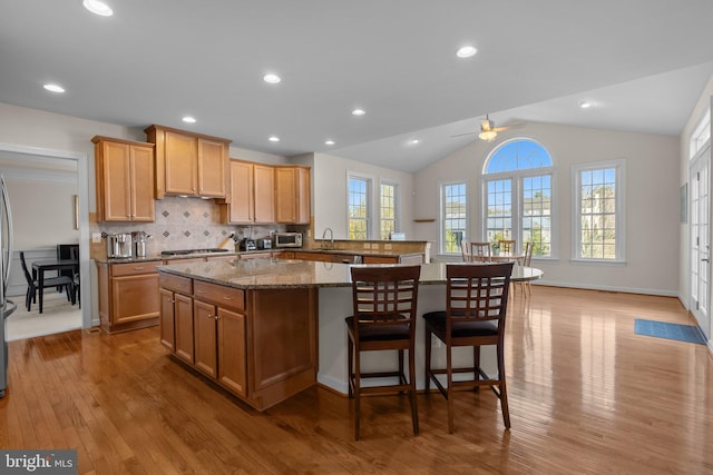 kitchen featuring a sink, a kitchen breakfast bar, a kitchen island, wood finished floors, and lofted ceiling