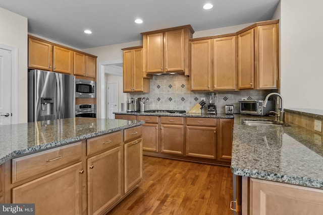 kitchen featuring decorative backsplash, dark stone countertops, appliances with stainless steel finishes, wood finished floors, and a sink