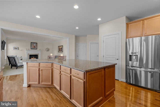 kitchen featuring stone countertops, open floor plan, a lit fireplace, stainless steel fridge with ice dispenser, and light wood finished floors