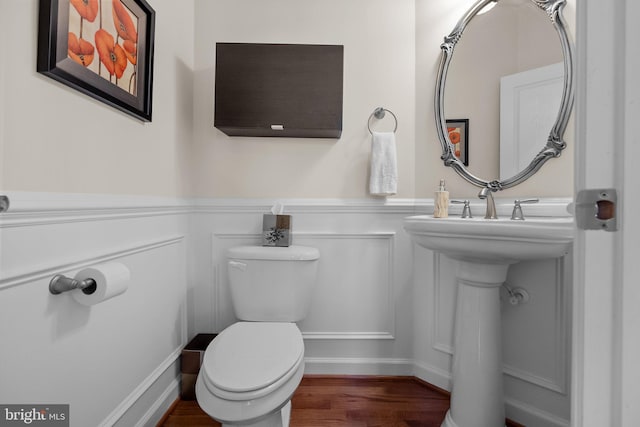 bathroom with a decorative wall, wainscoting, toilet, and wood finished floors