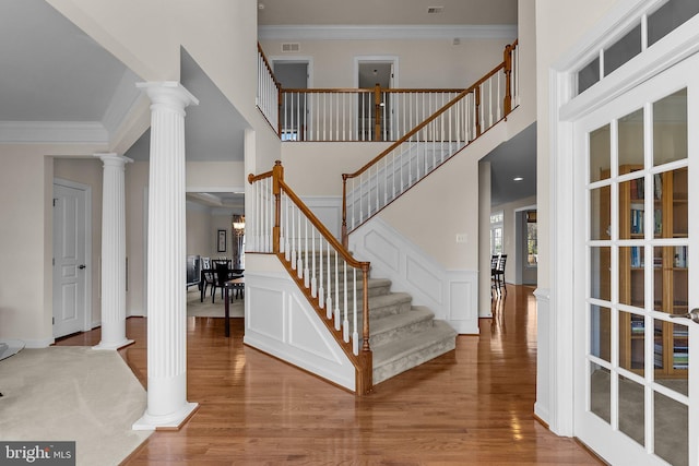 foyer featuring visible vents, wood finished floors, ornamental molding, and ornate columns