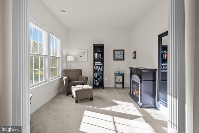 living area featuring light carpet, visible vents, baseboards, and a glass covered fireplace