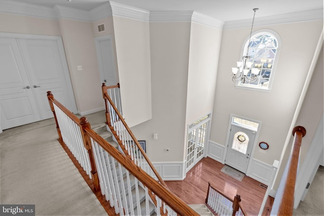 foyer featuring visible vents, ornamental molding, wainscoting, a decorative wall, and a notable chandelier