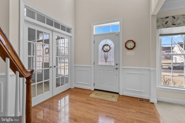 entryway with visible vents, light wood-style flooring, french doors, wainscoting, and a decorative wall