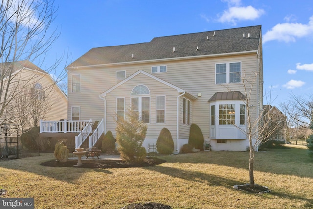 rear view of property with a patio, a wooden deck, a lawn, and a shingled roof