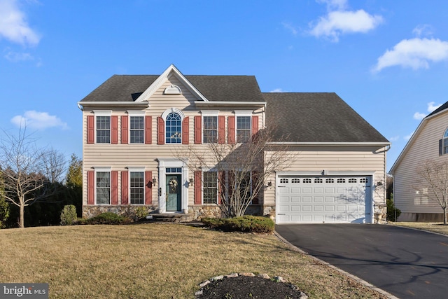 colonial inspired home with roof with shingles, an attached garage, a front lawn, stone siding, and aphalt driveway