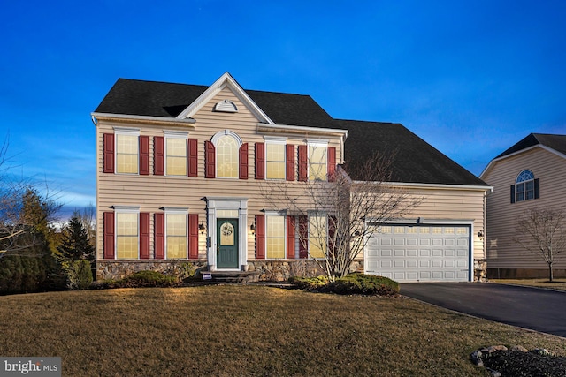 colonial-style house featuring a front lawn, an attached garage, and driveway