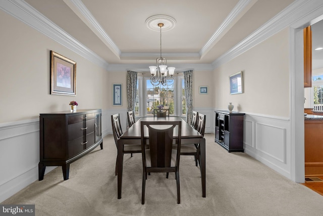 dining space featuring light carpet, a chandelier, a raised ceiling, and a wainscoted wall