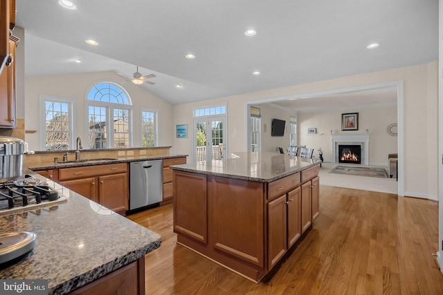 kitchen featuring lofted ceiling, a glass covered fireplace, stone countertops, stainless steel appliances, and a sink