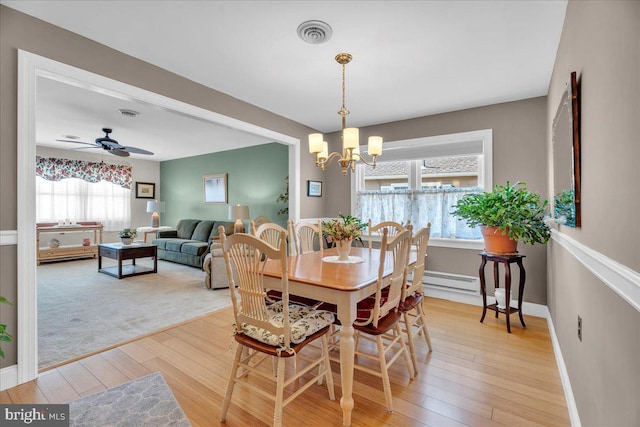 dining area with baseboards, visible vents, light wood-style flooring, ceiling fan with notable chandelier, and baseboard heating